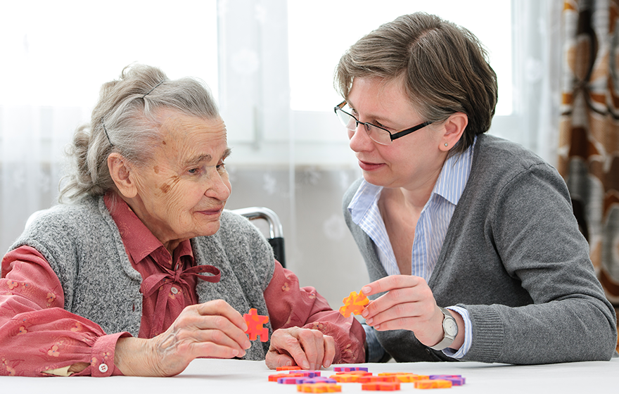 A personal care worker assisting an aging adult with a puzzle