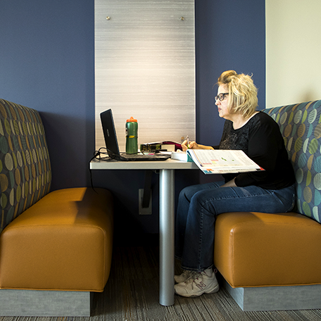 A student sitting in a table booth and studying with books and a laptop