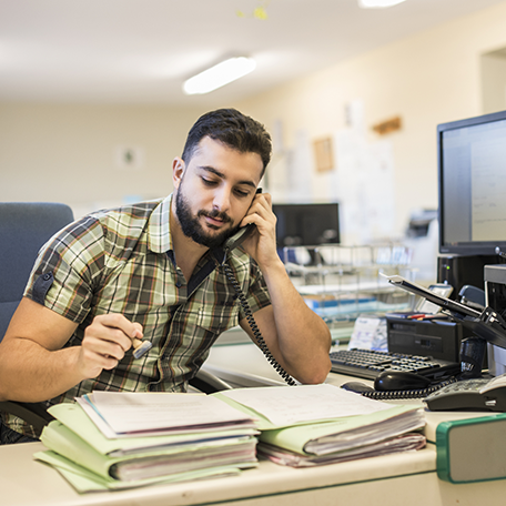 An office employee on the phone and looking at a stack of papers