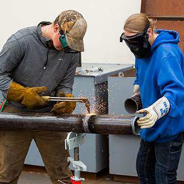 Two students welding a pipe