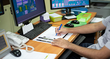 An employee in production control room. There is a computer in the control of machinery at feed mills