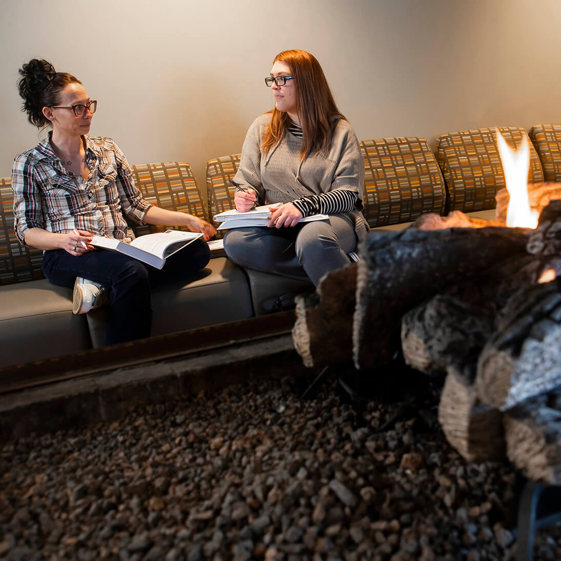 Two students sitting by a fireplace in a common area on campus