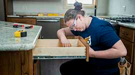 A student working on kitchen drawers in a house