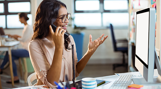 A graphic designer at the computer talking on the phone