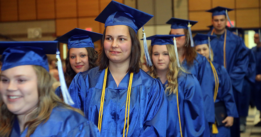 Northwood Tech students dressed in blue caps and gowns with yellow tassels walking in a line at graduation.