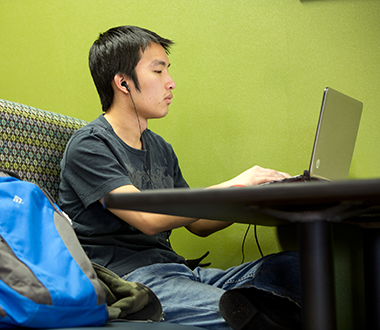 Student working on his computer Young, male student working on his computer in a booth on campus with headphones in.