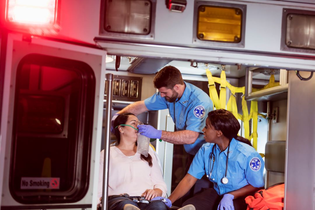 Two EMTs administering medical assistance to a patient in the back of an ambulance