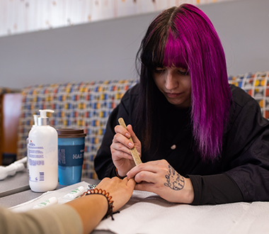 Cosmetology student practicing painting nails on another student