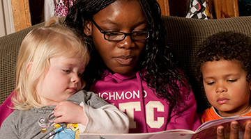 An early childhood educator reading a children's book to two toddlers