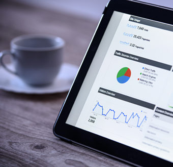 Image of a cup of coffee and an iPad on a table; the iPad is pulled up to a page that is viewing stocks