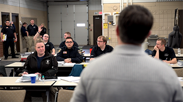 Students sitting at desks listening to an instructor in the front of the room