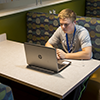 Young man sits at a booth in Ashland with headphones in and working at a laptop.