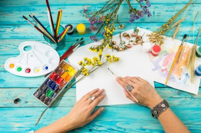 Colorful paint, brushes, blank paper on a table with hands of a painter ready to start a new project