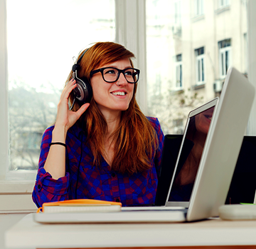A person sitting at a laptop wearing headphones and smiling