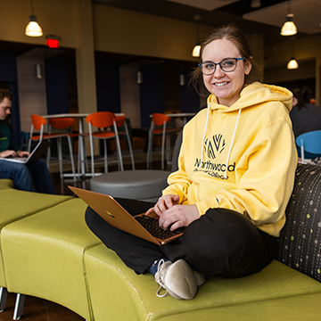 Image of a student sitting on campus couch working on her laptop