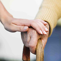 Close up of a hand on a cane and a caregiver's hand gently on top of the other hand