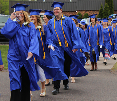 Graduates walk in line from the WITC-Ashland building with blue caps and gowns on.