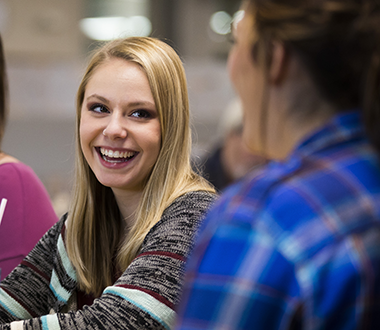 Young woman smiles at a friend while conversing at a table.