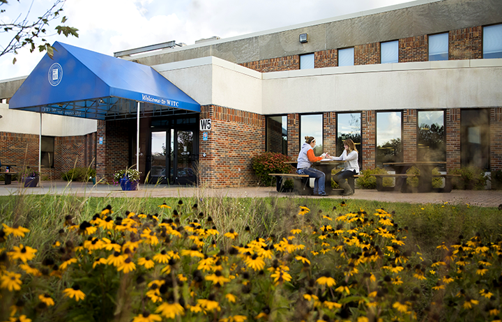Outside view of Rice Lake campus with two students sitting at a picnic table