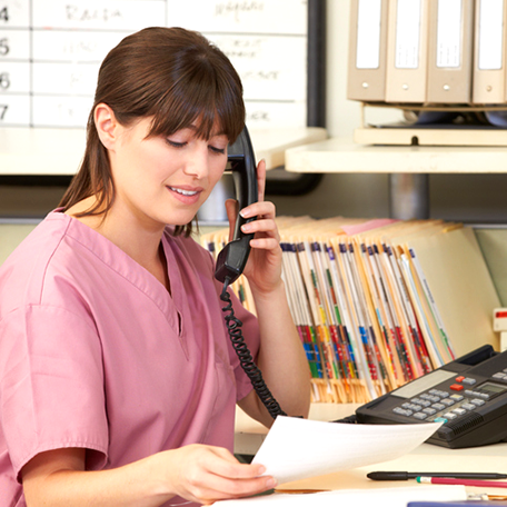 A medical professional talking on the phone with folders behind her