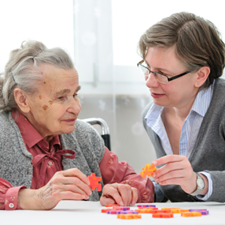 A personal caregiver assisting an aging adult with a puzzle