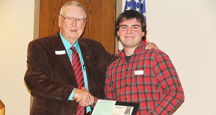 Elderly man in a suit presenting a student with a scholarship award.