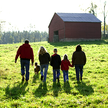 A family walking in a green field toward a farm