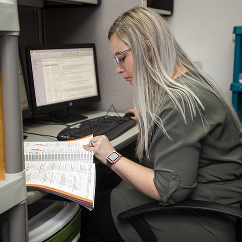 A medical administrative professional referencing a textbook in an office