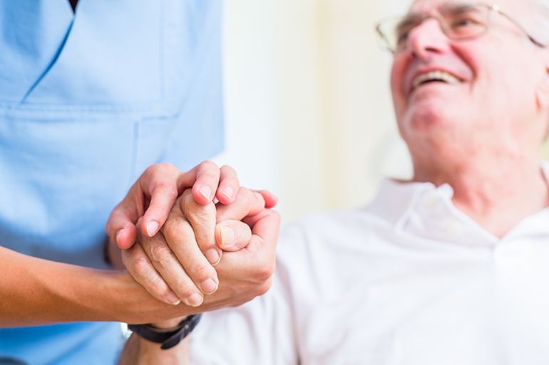 professional caregiver holding hand of smiling patient