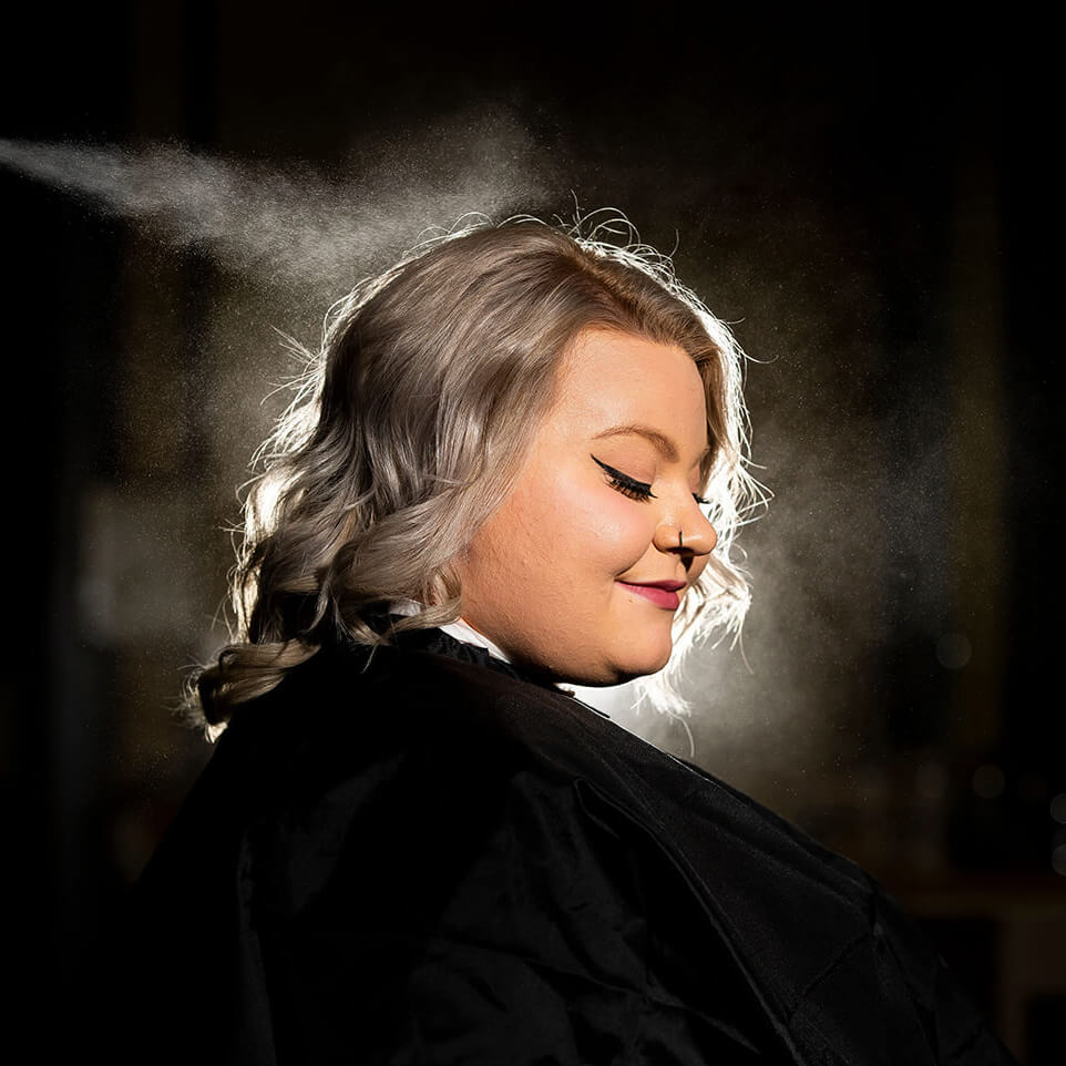 A cosmetology client having their hair sprayed