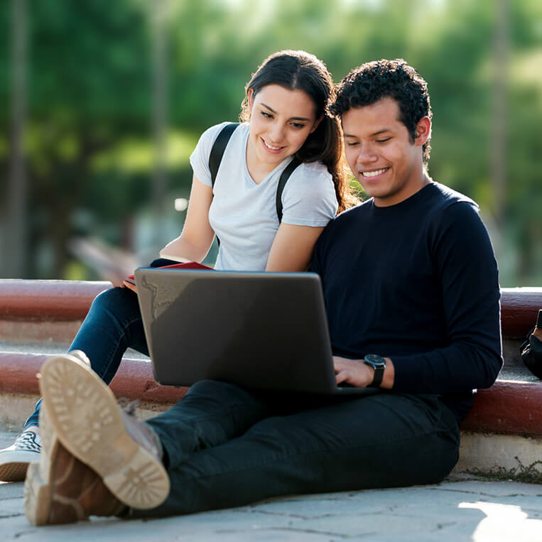 Two students sitting outside and doing school work on a laptop