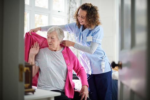 caregiver helping senior woman get dressed in her bedroom