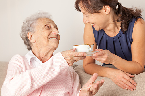 smiling daughter shares teas with elderly mother