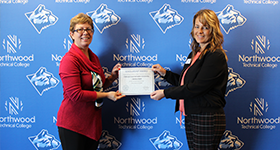 Director presenting a scholarship to a student in front of the Northwood Tech backdrop.