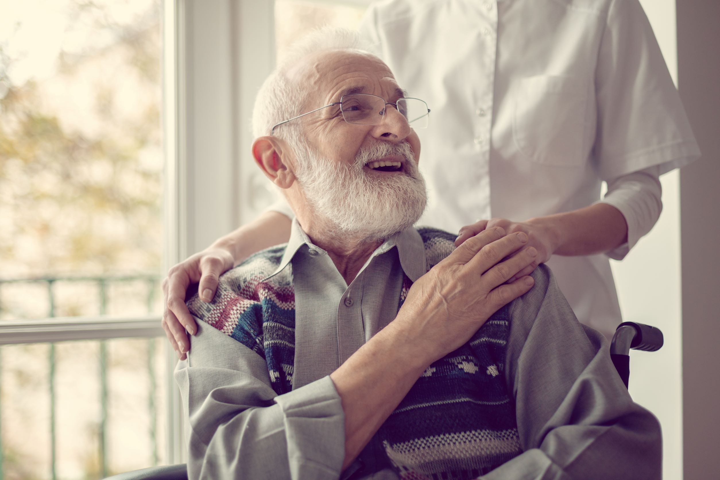 smiling elderly patient sitting in wheelchair with caregiver standing behind him