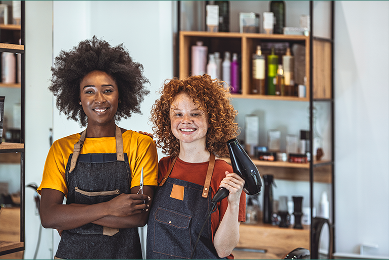 Two smiling cosmetology students standing side by side in a salon