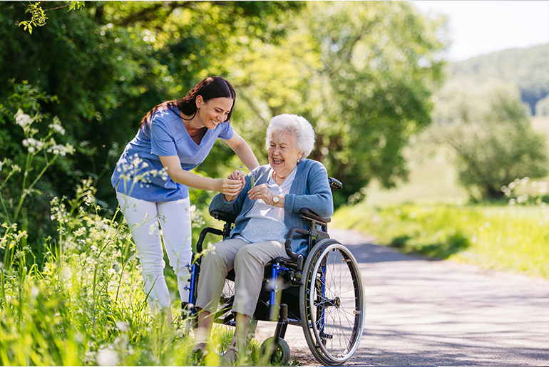 smiling caregiver and patient in wheelchair pick flowers on a sunny day