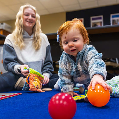 Toddler playing with pit balls in classroom with student