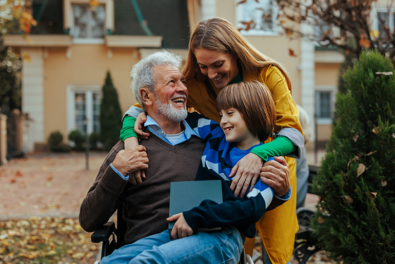 Grandfather in wheelchair smiling at daughter and granddaughter outside