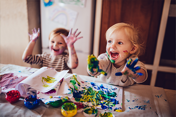 two smiling toddlers play in finger paints at a table