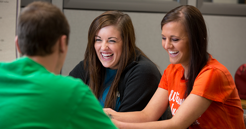 Students hanging out on campus two women laugh as they converse with another student across the table