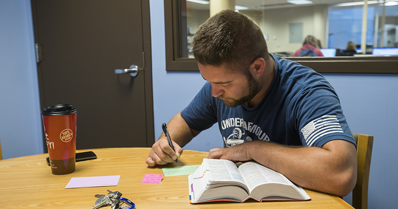 Students sitting in study room reading a book and taking notes on flash cards