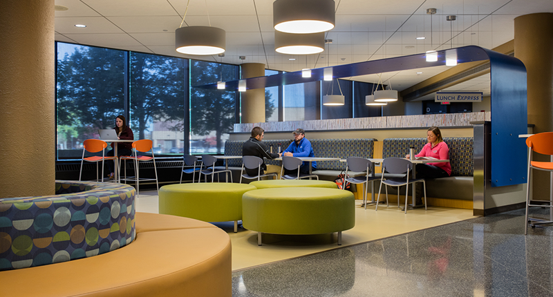 Students sit, study and chat at tables and booths in a modern setting at the WITC-Superior Campus in the atrium.