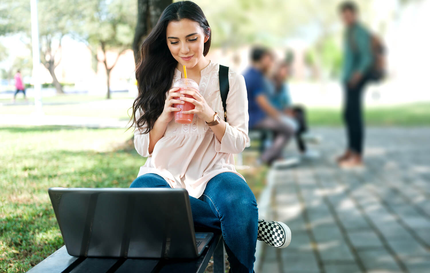 A student sitting outside with a laptop and a coffee