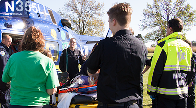 EMT students gathered around an instructor in front of a helicopter