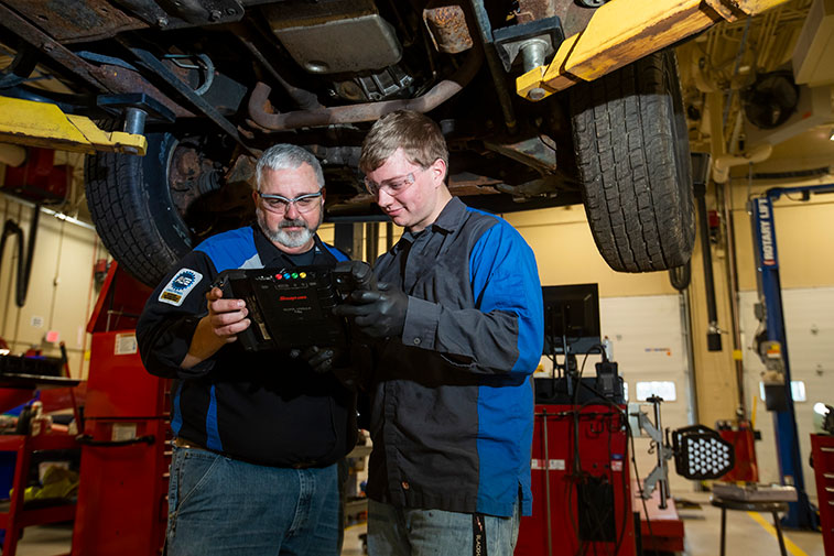 Automotive student with instructor examining the undercarriage of a truck