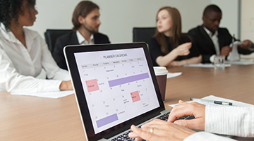 An administrative coordinator looking at a calendar on their computer while in a group meeting