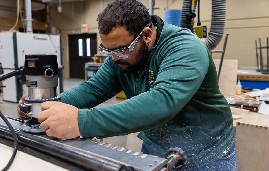 Person using a handheld router to shape wood in a workshop setting.