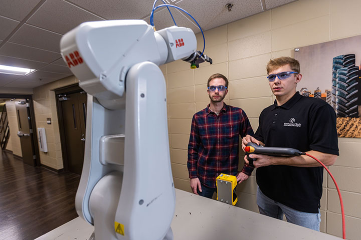 Two males working with a robotic arm, using a handheld controller.