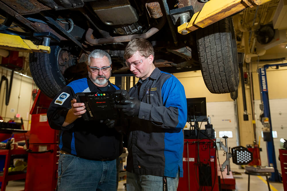 Automotive student with instructor examining the undercarriage of a truck
